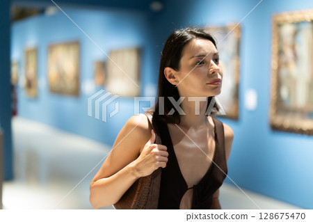 Young woman in summer clothes looking at paintings in museum Young woman in summer clothes looking at paintings in museum 128675470