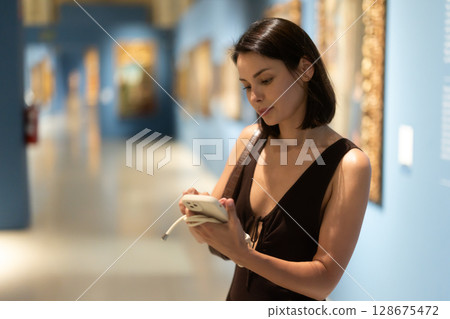 While visiting museum, girl uses travel guide application on her phone. 128675472