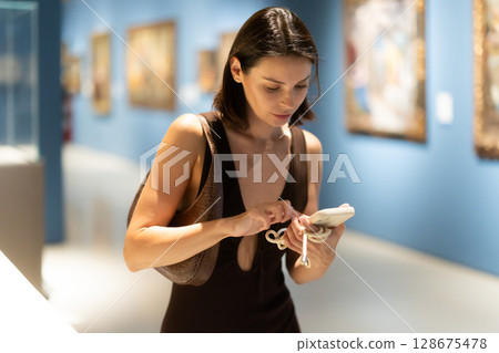 Young woman in summer clothes looking at paintings in museum 128675478
