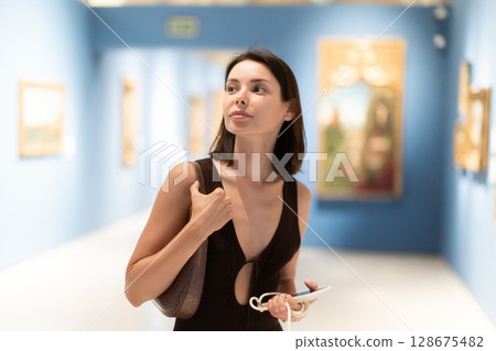 Young woman in summer clothes looking at paintings in museum 128675482