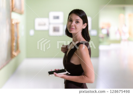 young woman with a phone in her hands visits a museum young woman with a phone in her hands visits a museum 128675498