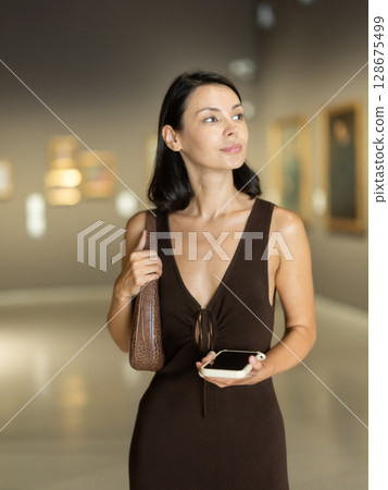 Woman visiting museum and looking at paintings in gold frames 128675499