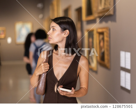 Woman visiting museum and looking at paintings in gold frames 128675501