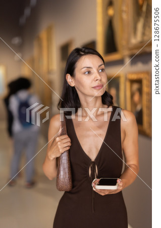 Woman with phone in hands in museum hall, view painting exhibition 128675506