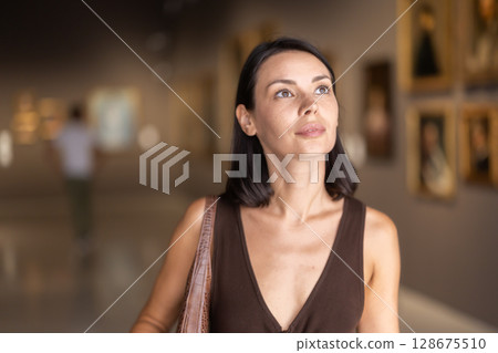 Woman visiting museum and looking at paintings in gold frames 128675510