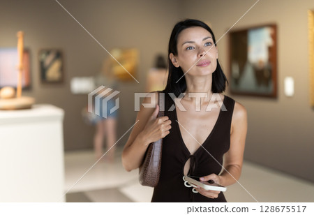 Woman with phone in hands in museum hall, view painting exhibition 128675517