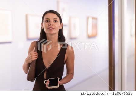 Young female visitor stands near glass display case in museum Young female visitor stands near glass display case in museum 128675525