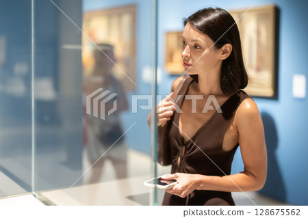 Young female visitor stands near glass display case in museum 128675562