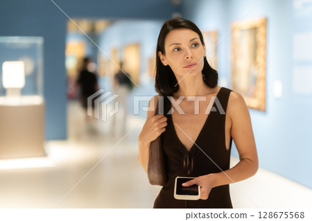 Young woman in summer clothes looking at paintings in museum 128675568