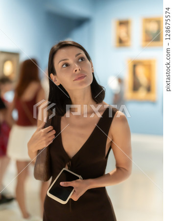 Woman visiting museum and looking at paintings in gold frames Woman visiting museum and looking at paintings in gold frames 128675574