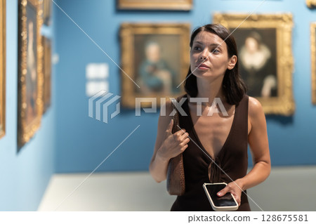 Woman with phone in hands in museum hall, view painting exhibition 128675581