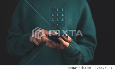 Person dialing on a smartphone with a futuristic virtual keypad interface hovering, symbolizing advanced communication. Concept of digital security and data protection on mobile devices. Person dialing on a smartphone with a futuristic virtual keypad interface hovering, symbolizing advanced communication. Concept of digital security and data protection on mobile devices. 128675984