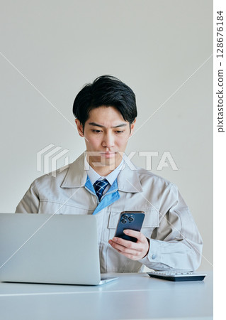 一名身穿工作服的年輕男子正在操作智慧型手機 128676184