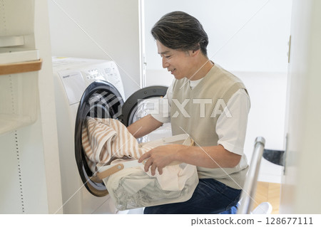 A man in his 50s putting laundry into a washing machine A man in his 50s putting laundry into a washing machine 128677111
