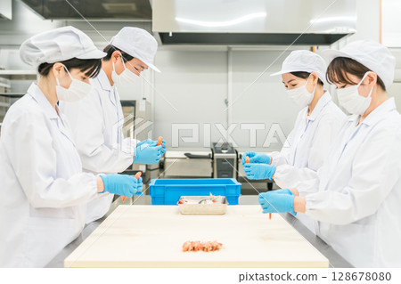 Male and female staff in sanitary clothing preparing ingredients and cooking 128678080