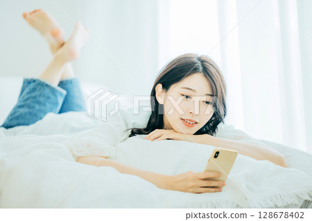 一名婦女在床上的看一個智能手機 128678402
