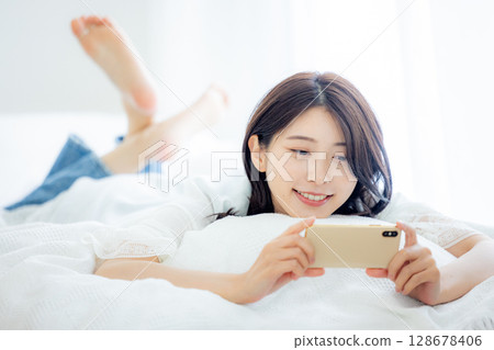 一名婦女在床上的看一個智能手機 128678406