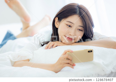 一名婦女在床上的看一個智能手機 128678407