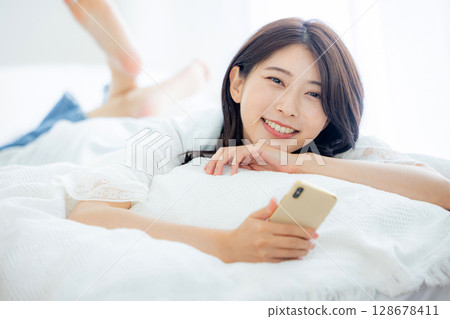 一名婦女在床上的看一個智能手機 128678411