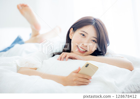 一名婦女在床上的看一個智能手機 128678412