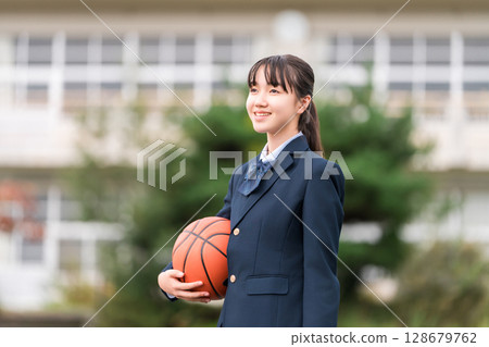 High school, junior high school, and elementary school girls in uniform standing in a schoolyard holding a basketball 128679762