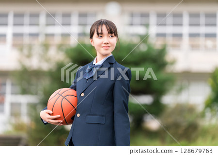 High school, junior high school, and elementary school girls in uniform standing in a schoolyard holding a basketball 128679763