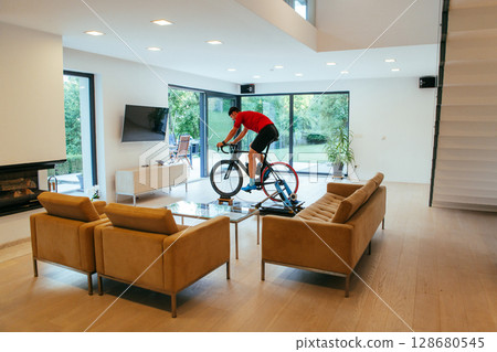 A triathlete riding a triathlon bike on a machine simulation in a modern living room 128680545