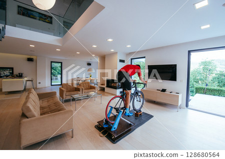 A triathlete riding a triathlon bike on a machine simulation in a modern living room 128680564