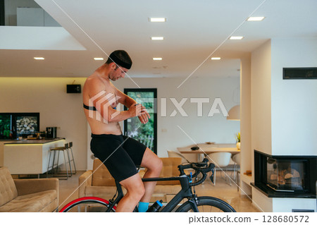 A triathlete riding a triathlon bike on a machine simulation in a modern living room A triathlete riding a triathlon bike on a machine simulation in a modern living room 128680572