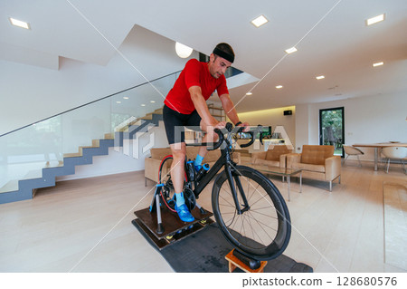 A triathlete riding a triathlon bike on a machine simulation in a modern living room 128680576