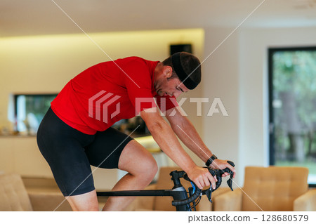 A triathlete riding a triathlon bike on a machine simulation in a modern living room 128680579