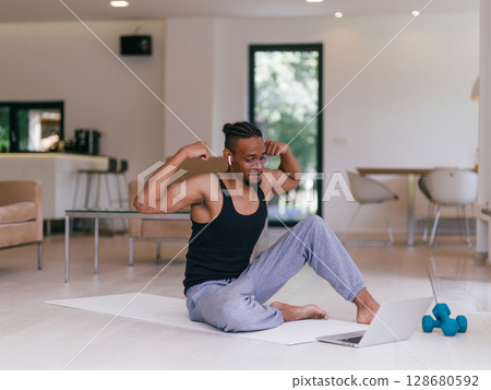 Training At Home. Sporty man doing the training while watching an online tutorial on a laptop, exercising in the living room, free space. Training At Home. Sporty man doing the training while watching an online tutorial on a laptop, exercising in the living room, free space. 128680592