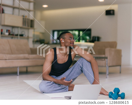Training At Home. Sporty man doing the training while watching an online tutorial on a laptop, exercising in the living room, free space. Training At Home. Sporty man doing the training while watching an online tutorial on a laptop, exercising in the living room, free space. 128680615