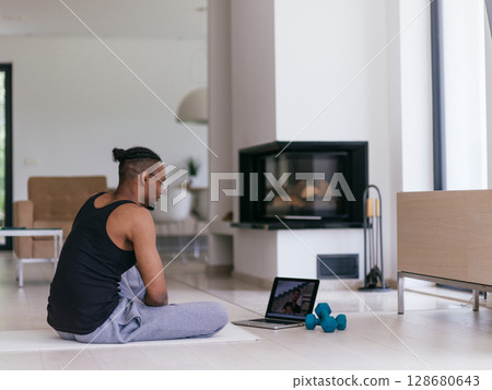 Training At Home. Sporty man doing the training while watching an online tutorial on a laptop, exercising in the living room, free space. Training At Home. Sporty man doing the training while watching an online tutorial on a laptop, exercising in the living room, free space. 128680643