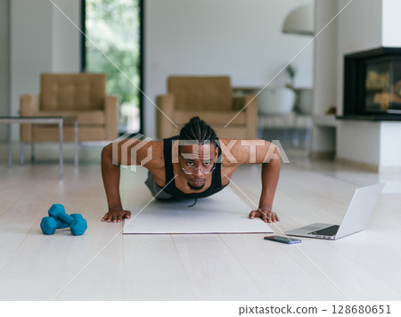 Training At Home. Sporty man doing the training while watching an online tutorial on a laptop, exercising in the living room, free space. Training At Home. Sporty man doing the training while watching an online tutorial on a laptop, exercising in the living room, free space. 128680651