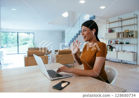Woman sitting in living room using laptop looking at cam talk by video call with business friend relatives, head shot. Job interview answering questions Woman sitting in living room using laptop looking at cam talk by video call with business friend relatives, head shot. Job interview answering questions 128680734