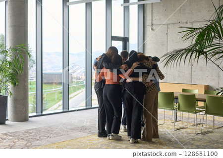 A diverse group of professionals standing in a supportive circle, embracing each other in a modern office space filled with natural light. A diverse group of professionals standing in a supportive circle, embracing each other in a modern office space filled with natural light. 128681100