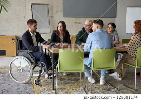 A diverse group of business professionals sitting in an office meeting with their director, who is in a wheelchair, fostering collaboration, leadership, and inclusivity A diverse group of business professionals sitting in an office meeting with their director, who is in a wheelchair, fostering collaboration, leadership, and inclusivity 128681174