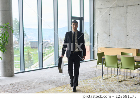 A determined businessman in a black suit confidently walks through the office, embodying professionalism and focus as he heads towards new challenges A determined businessman in a black suit confidently walks through the office, embodying professionalism and focus as he heads towards new challenges 128681175