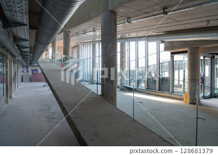 A captivating view of a modern business building under construction, showcasing its raw industrial interior with exposed steel beams and concrete walls bathed in the warm, golden hues of a sunset A captivating view of a modern business building under construction, showcasing its raw industrial interior with exposed steel beams and concrete walls bathed in the warm, golden hues of a sunset 128681379