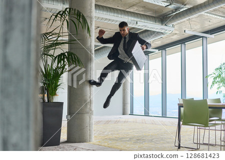 A businessman ecstatically jumping in a modern office, holding a briefcase in his hands, celebrating a moment of success and triumph. 128681423