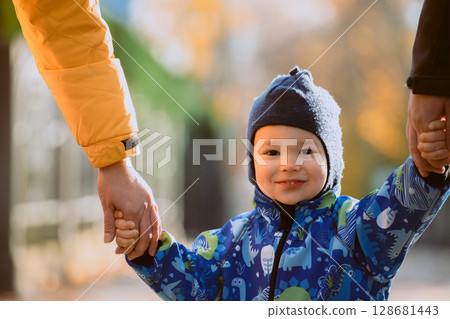 Parents walking hand in hand with their son through the charming city streets, enjoying the warmth of the season and creating joyful memories together Parents walking hand in hand with their son through the charming city streets, enjoying the warmth of the season and creating joyful memories together 128681443