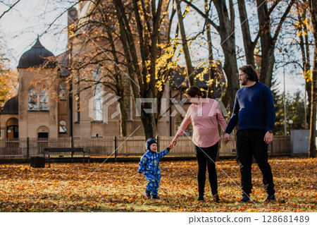 A loving couple strolls through a sunlit park with their young son, surrounded by the vibrant colors of autumn, enjoying a joyful and peaceful family moment together. 128681489