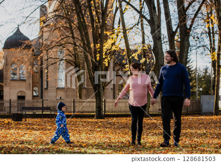 A loving couple strolls through a sunlit park with their young son, surrounded by the vibrant colors of autumn, enjoying a joyful and peaceful family moment together. A loving couple strolls through a sunlit park with their young son, surrounded by the vibrant colors of autumn, enjoying a joyful and peaceful family moment together. 128681503