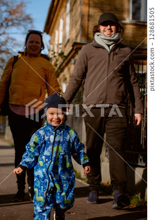 A loving couple strolls through a sunlit park with their young son, surrounded by the vibrant colors of autumn, enjoying a joyful and peaceful family moment together. 128681505