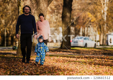 A loving couple strolls through a sunlit park with their young son, surrounded by the vibrant colors of autumn, enjoying a joyful and peaceful family moment together. A loving couple strolls through a sunlit park with their young son, surrounded by the vibrant colors of autumn, enjoying a joyful and peaceful family moment together. 128681512