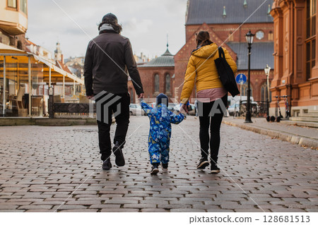 Parents walking hand in hand with their son through the charming city streets, enjoying the warmth of the season and creating joyful memories together Parents walking hand in hand with their son through the charming city streets, enjoying the warmth of the season and creating joyful memories together 128681513