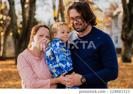On a sunny autumn day in the park, a mother and father lovingly embrace their young son, sharing moments of laughter and joy as they play together On a sunny autumn day in the park, a mother and father lovingly embrace their young son, sharing moments of laughter and joy as they play together 128681523