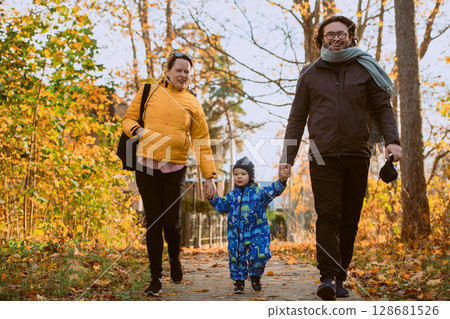 A loving couple strolls through a sunlit park with their young son, surrounded by the vibrant colors of autumn, enjoying a joyful and peaceful family moment together. A loving couple strolls through a sunlit park with their young son, surrounded by the vibrant colors of autumn, enjoying a joyful and peaceful family moment together. 128681526