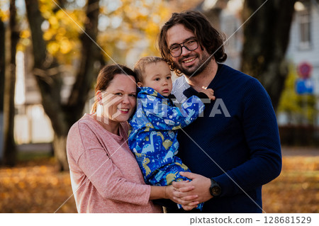 On a sunny autumn day in the park, a mother and father lovingly embrace their young son, sharing moments of laughter and joy as they play together On a sunny autumn day in the park, a mother and father lovingly embrace their young son, sharing moments of laughter and joy as they play together 128681529